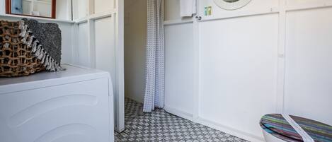 Een badkamer met een witte wasmachine, een douche met een gordijn met stippen, een ronde spiegel en een betegelde vloer.