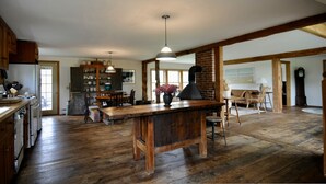 A spacious kitchen with wooden floors, a central island, and a brick wall. There are hanging lights and a large window providing natural light. - Long View Farm on Broad Bay (Waldoboro)