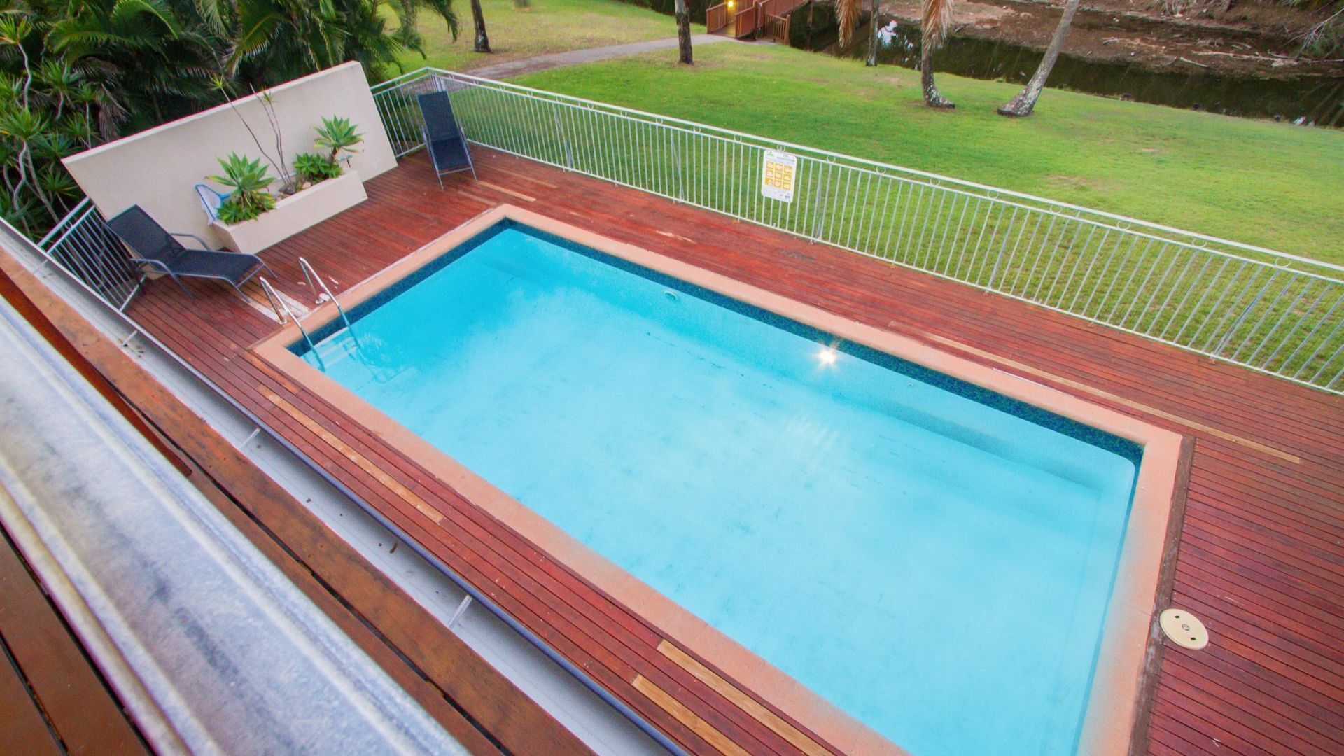 Une piscine rectangulaire dotée d’une terrasse en bois et d’une clôture en métal.