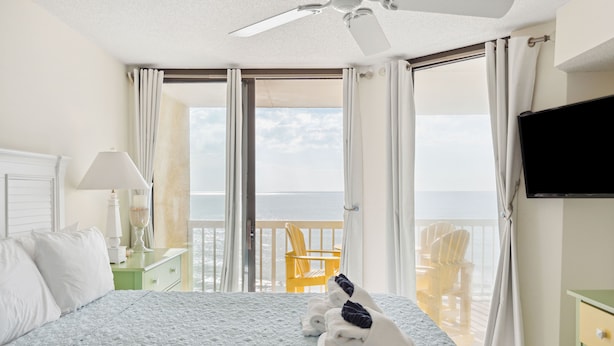 Habitación de hotel con cama, televisión, balcón con sillas y vista al mar.