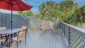 A wooden deck with a table and chairs, a red umbrella, and a wooden fence. - Charming Cottage worth every $$ (Delray Beach)