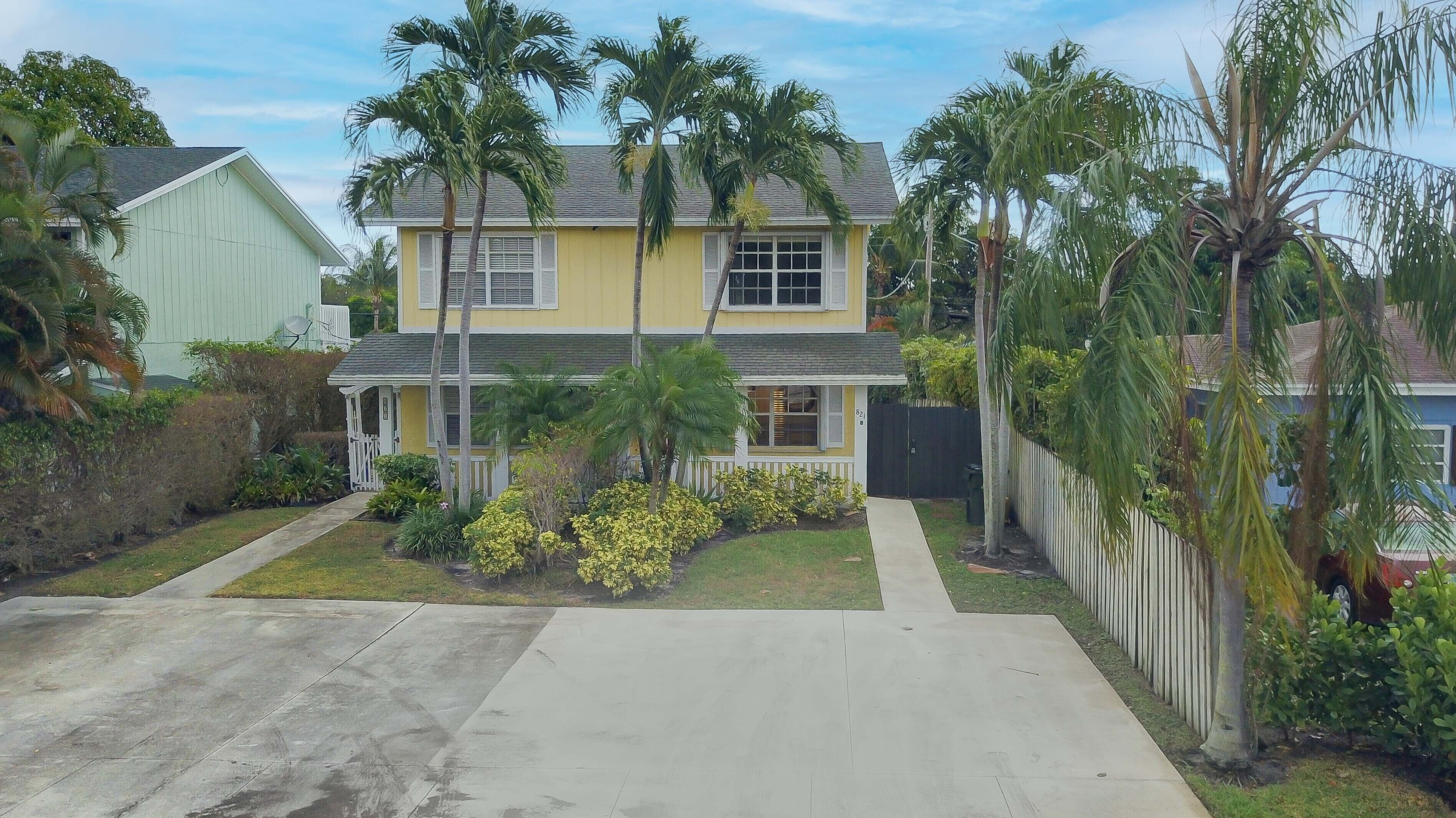 A two-story house with a front porch, surrounded by palm trees and a well-maintained lawn.