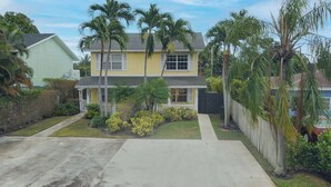 A two-story house with a front porch, surrounded by palm trees and a well-maintained lawn. - Charming Cottage worth every $$ (Delray Beach)