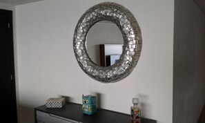 Um espelho com padrão de mosaico numa parede, um penteado com uma caixa, uma coruja em vidro azul e uma garrafa de vidro.