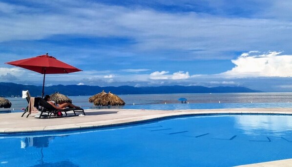Piscina com vista clara para o mar e montanhas ao fundo.