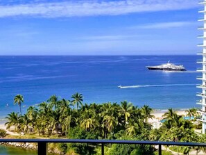 Um hotel à beira-mar com vista para o oceano e um navio de cruzeiro ao longe.