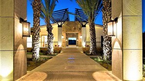 Un camino conduce a la entrada de un edificio, con palmeras e iluminación exterior.