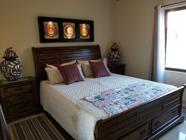 A neatly made bed with a quilt, two decorative vases, a wooden headboard, and a window with curtains.