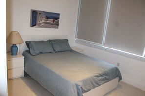 A bedroom with a bed, a nightstand, a lamp, and a window.