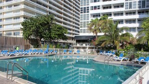 Ein Hotelpoolbereich mit klarem Wasser, blauen Liegestühlen und einer Palme.