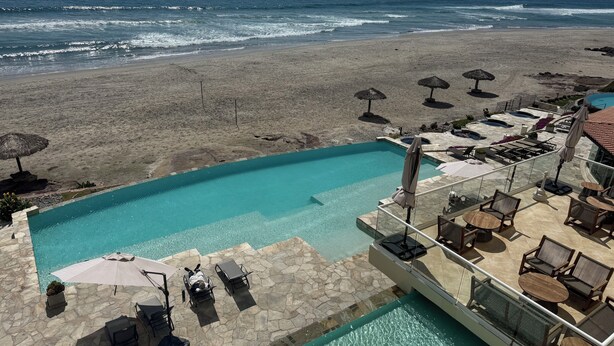 A pool area with lounge chairs and umbrellas, a beach in the background, and a clear view of the ocean. - Stunning, Relaxing Beachfront With Endless Activities & Enjoyment (Rosarito)