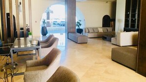 A spacious lobby with a modern design, featuring a seating area with sofas and armchairs, a glass coffee table, and a view through an arched doorway. - Stunning, Relaxing Beachfront With Endless Activities & Enjoyment (Rosarito)