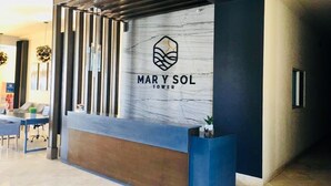 A reception desk with a logo, a modern design, and a seating area in the background. - Stunning, Relaxing Beachfront With Endless Activities & Enjoyment (Rosarito)