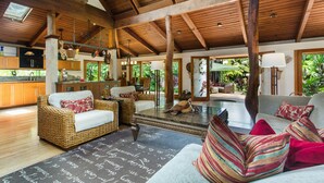 A spacious living area with wicker furniture, a fireplace, and a view of the outdoors. - Resort-like, 200 meters to Lanikai Beach, Private Pool, AC, Tropical Retreat (Kailua)