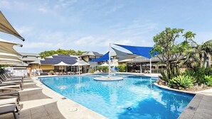 A swimming pool with lounge chairs, a water fountain, and a covered area with solar panels. - Broadwater Bliss—Beachside Escape w/ Resort Perks (Broadwater)
