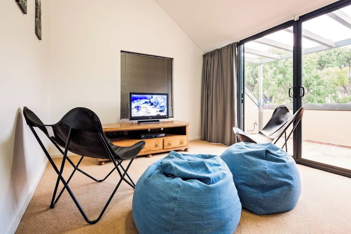 A modern living room with a television, two bean bag chairs, and a sliding glass door to a balcony.