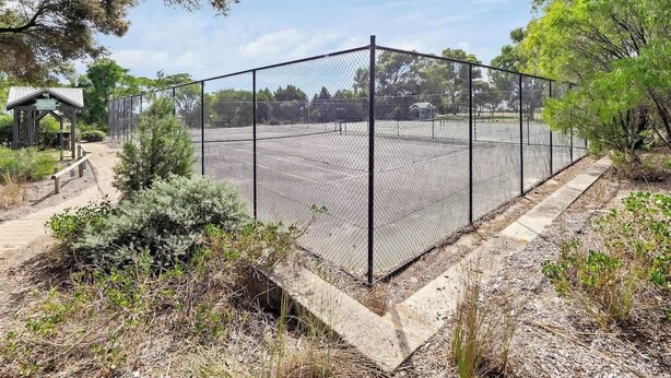 A fenced tennis court with a wooden pavilion and a dirt path. - Broadwater Bliss—Beachside Escape w/ Resort Perks (Broadwater)
