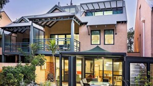 A modern two-story house with a balcony, large windows, and a well-maintained garden. - Broadwater Bliss—Beachside Escape w/ Resort Perks (Broadwater)
