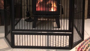 Estufa de metal negro con fuego encendido en su interior, rodeada por una valla de metal negro.