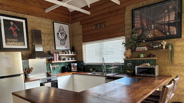 Una cocina con una isla de madera, armarios blancos, un refrigerador de acero inoxidable, un microondas y un fregadero.