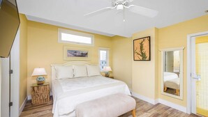 Un dormitorio con cama, mesitas de noche, un banco, ventilador de techo y una puerta con espejo.