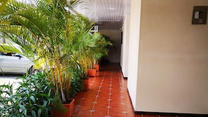 A hallway with red tiled flooring, potted plants, and a white car parked on the left. - Hotel Amaranto (San Juan)