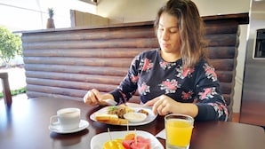 A person seated at a table with a plate of food, a cup of coffee, and a glass of orange juice. - Hotel Amaranto (San Juan)