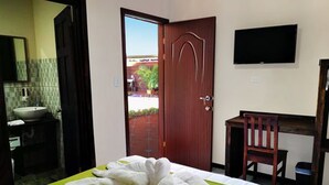 A hotel room with a bed, a desk, a chair, a television, and a bathroom with a sink and mirror. - Hotel Amaranto (San Juan)