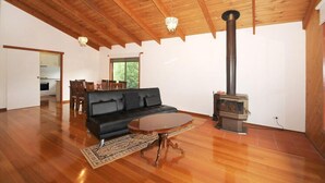 A spacious living room with a black sofa, a wooden coffee table, and a wood-burning stove.