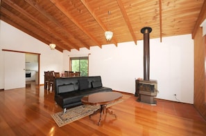 A spacious living room with a black sofa, a wooden coffee table, and a wood-burning stove.