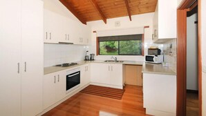 A modern kitchen with white cabinets, a wooden ceiling, and a window overlooking greenery.