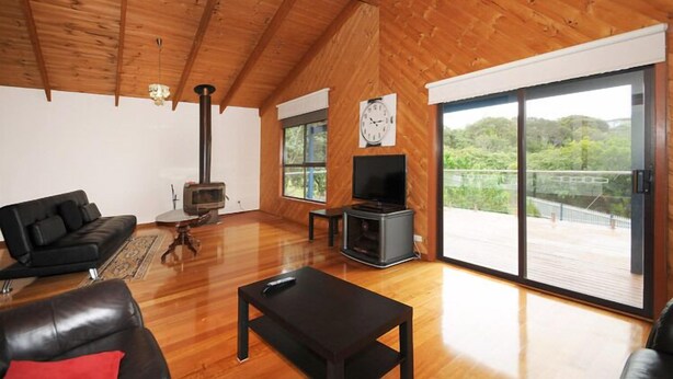 A spacious living area with a wooden ceiling, a fireplace, a television, and large sliding glass doors offering a view of greenery.