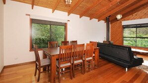 A dining area with a wooden table and chairs, a sofa, and large windows with a view of greenery.