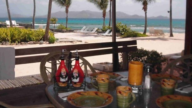 Zona pranzo in riva al mare con vista sull'oceano, palme e poltrone relax.