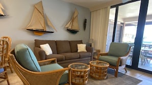 Un soggiorno con divano, due poltrone in vimini, un tavolino da caffè e una grande finestra con vista.