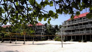 Una spiaggia con un campo da pallavolo, una rete, palme e un edificio con balconi sullo sfondo.