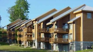Une rangée d’immeubles en bois à plusieurs étages, dotés de balcons, qui font probablement partie d’un hôtel ou d’un complexe touristique.