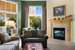 A living room with a fireplace, a sofa, a coffee table, and a view of trees through a window.