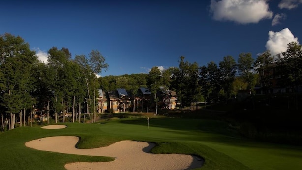 Un parcours de golf avec des bunkers de sable, des arbres et des immeubles résidentiels en arrière-plan.