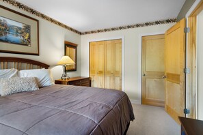 A bedroom with a large bed, a nightstand, a lamp, a dresser, and a wardrobe.
