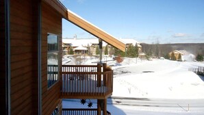 Un balcon en bois offrant une vue sur un paysage enneigé et sur des bâtiments en arrière-plan.