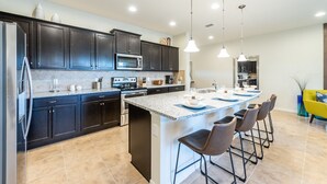 A modern kitchen with dark cabinets, a large island with bar stools, a microwave, and a refrigerator. - Brand new villa in amazing resort (Kissimmee)