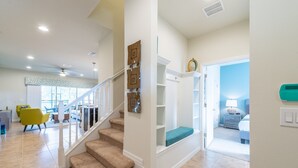 A modern interior with a staircase leading to a second floor, a dining area with yellow chairs, and a bedroom with a blue wall and a nightstand. - Brand new villa in amazing resort (Kissimmee)