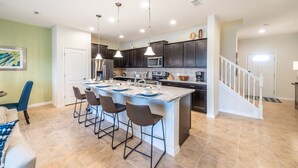 A modern kitchen with a central island, bar stools, and dark cabinetry. - Brand new villa in amazing resort (Kissimmee)