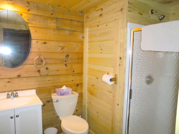 A wooden cabin bathroom with a toilet, sink, and a shower area.