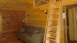 Interior de una cabaña de madera con zona de altillo, un sofá y una escalera.