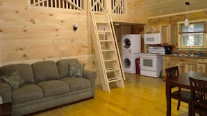 Interior acogedor de una cabaña con piso de madera, un sofá, una mesa de comedor y una zona de cocina que incluye una lavadora.