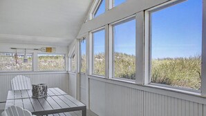 Un espace extérieur abrité, doté d’une table et de chaises, de grandes fenêtres et offrant une vue sur la plage.