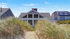 A house with a gabled roof, surrounded by sand dunes and tall grasses. - Oceanside 1 -  East Sandwich waterfront cottage (Sandwich/East Sandwich)