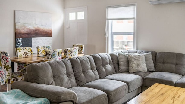 En stue med en grå modulsofa, et træbord og stole med blomstermønster.